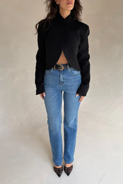 A woman wears the Charlotte Cropped Blazer Top Black with high-waisted blue jeans and pointed-toe mesh heels in a minimalist studio setting.