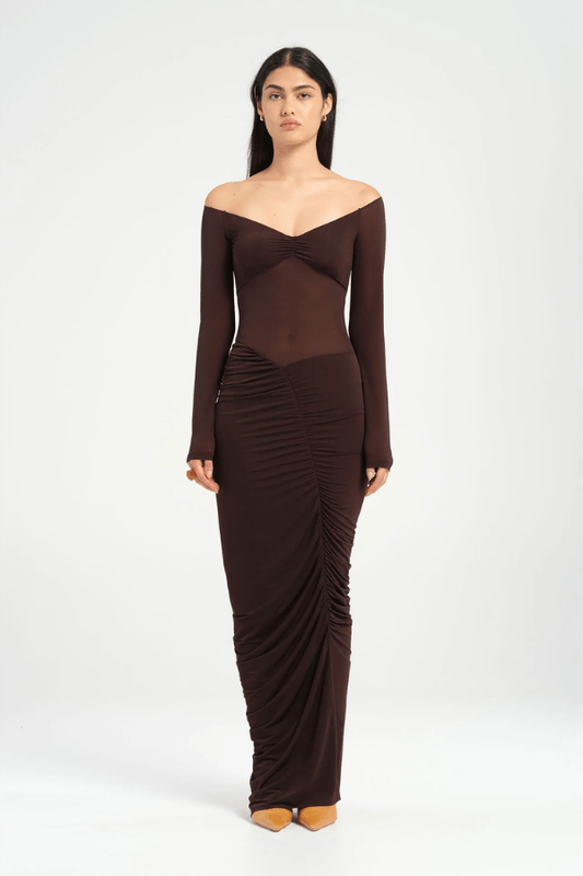 Wilma Maxi Dress Chocolate by Benni, featuring an off-shoulder V-neckline, full-length sleeves, sheer waist, and asymmetrical drape for a sculpted silhouette. Ideal for statement evenings.