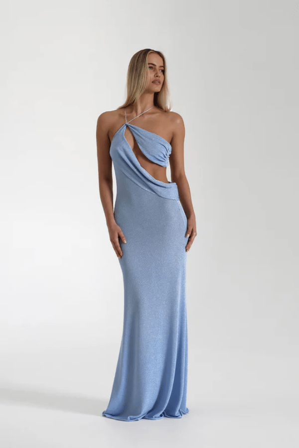 Elissa Dress Periwinkle by Natalie Rolt – A shimmering stretch-knit gown with metallic threads, asymmetrical cutaway, and flowing silhouette, perfect for sophisticated evening events and special occasions.