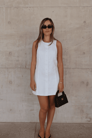 Mia Mini Dress White by Sneaky Link – A trendy, breathable linen dress with a high scoop neckline and button front, perfect for effortless summer days.
