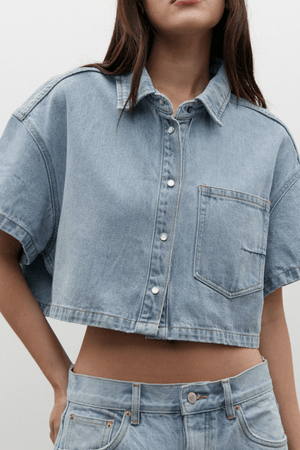 Zara Cropped Denim Shirt Oakland Blue by Bayse, a trendy cropped denim shirt with a relaxed fit and snap-button front. Perfect for effortless styling, whether paired with high-waisted denim or layered over a fitted tank.