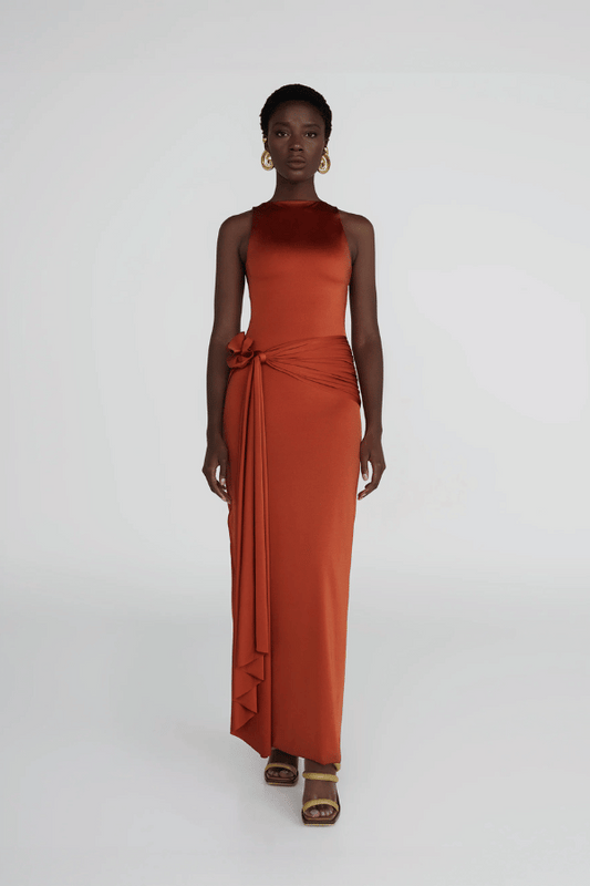 Tirso Terracotta by Maygel Coronel – Long dress with round neck, open back, ruched sash, and 3D flowers for elegant look.