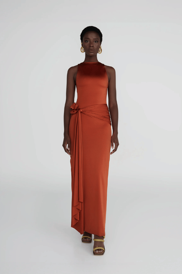 Tirso Terracotta by Maygel Coronel – Long dress with round neck, open back, ruched sash, and 3D flowers for elegant look.