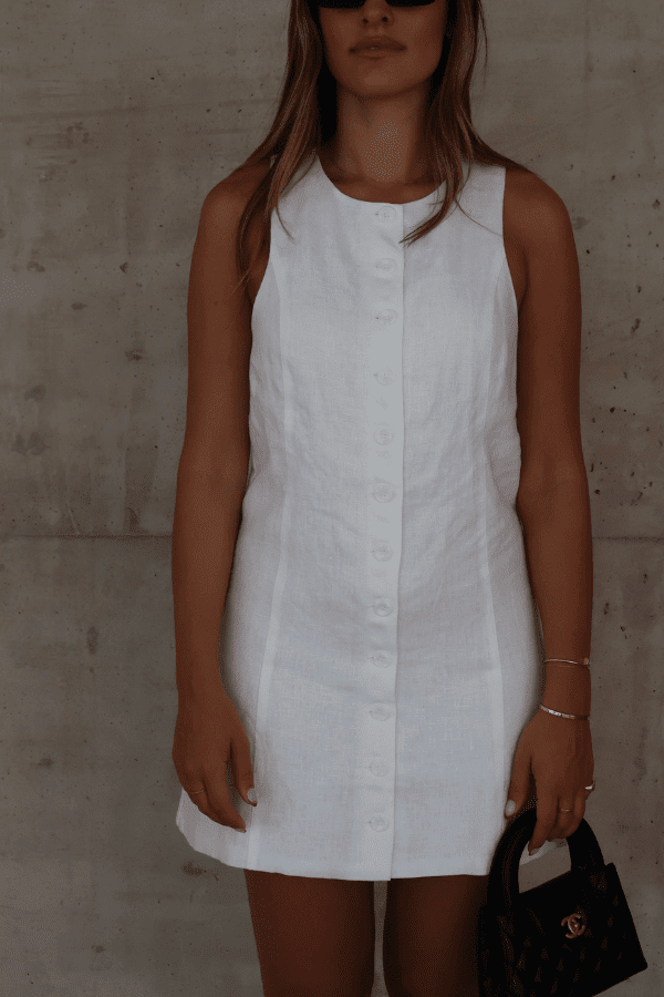 Mia Mini Dress White by Sneaky Link – A trendy, breathable linen dress with a high scoop neckline and button front, perfect for effortless summer days.
