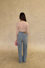 The Polly Long Sleeve top in pink. Woman in a pink top and white pants standing outside a store with plants and a bench in the background.