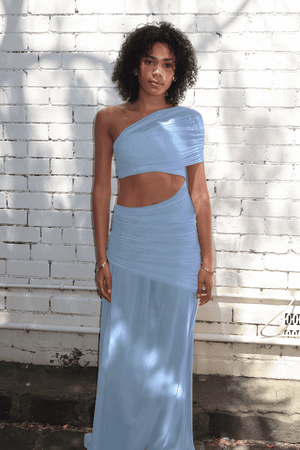 Tiana Dress Baby Blue by DŽO – Trendy one-shoulder sheer mesh maxi with asymmetrical draping, waist cutout, and pleated skirt, perfect for elegant day-to-evening occasions.