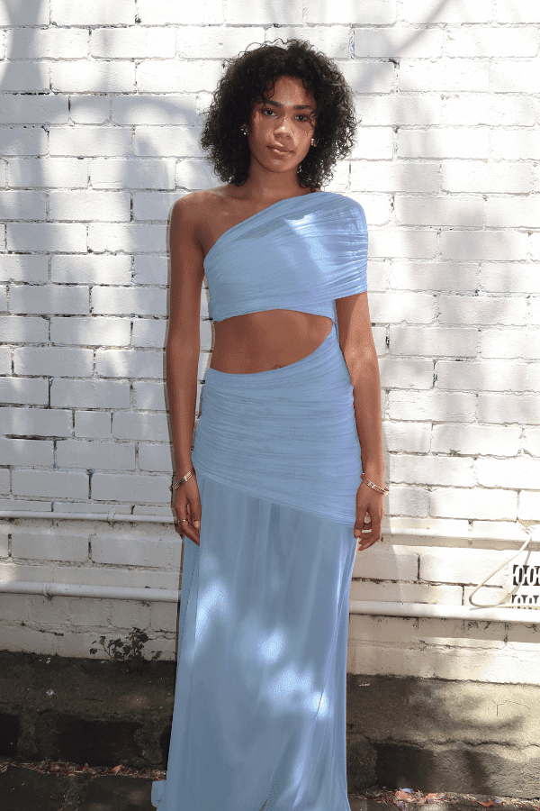 Tiana Dress Baby Blue by DŽO – Trendy one-shoulder sheer mesh maxi with asymmetrical draping, waist cutout, and pleated skirt, perfect for elegant day-to-evening occasions.
