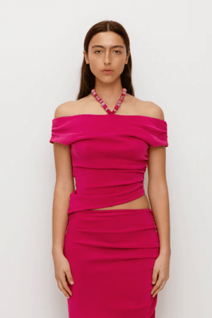 Flor Top Magenta by The Wolf Gang — an elegant event-ready top with asymmetric neckline, soft jersey fabric, and delicate beaded strap. True to size, perfect for casual or bold looks.