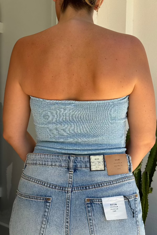 Woman wearing a denim strapless top and jeans standing in front of a mirror.