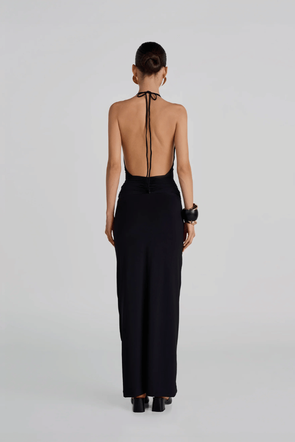 Lirio Maxi Dress Black by Maygel Coronel – A deep-V halter maxi with ruched waist, open back, and 3D floral detail for summer elegance.
