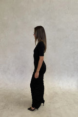 The Imana Draped Maxi Dress in Black by Sneaky Link features a flattering draped skirt, fitted upper, and soft modal stretch fabric for a feminine, timeless silhouette.