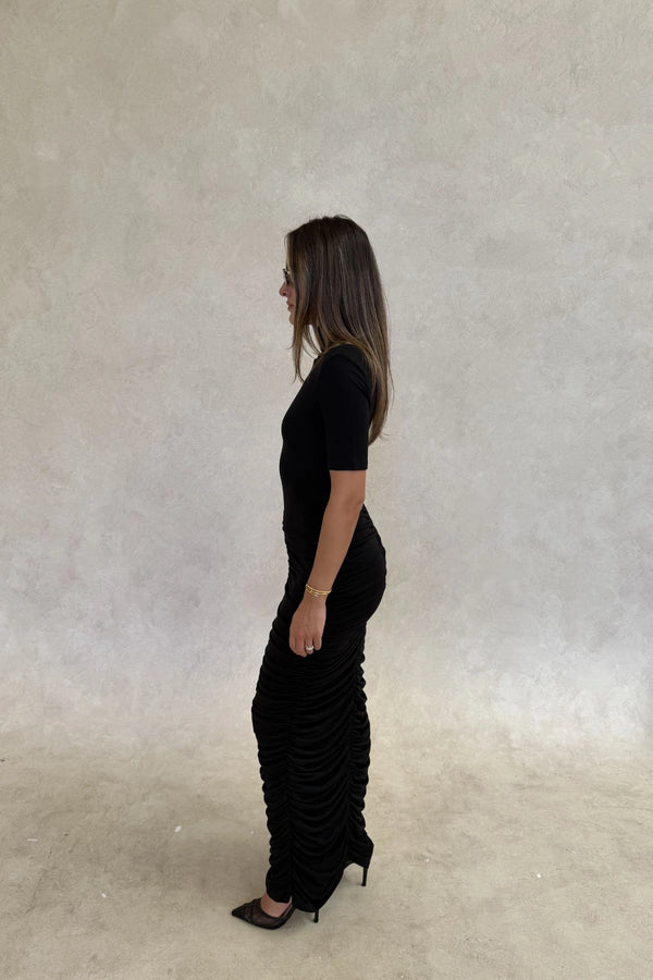 The Imana Draped Maxi Dress in Black by Sneaky Link features a flattering draped skirt, fitted upper, and soft modal stretch fabric for a feminine, timeless silhouette.