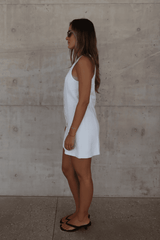 Mia Mini Dress White by Sneaky Link – A trendy, breathable linen dress with a high scoop neckline and button front, perfect for effortless summer days.