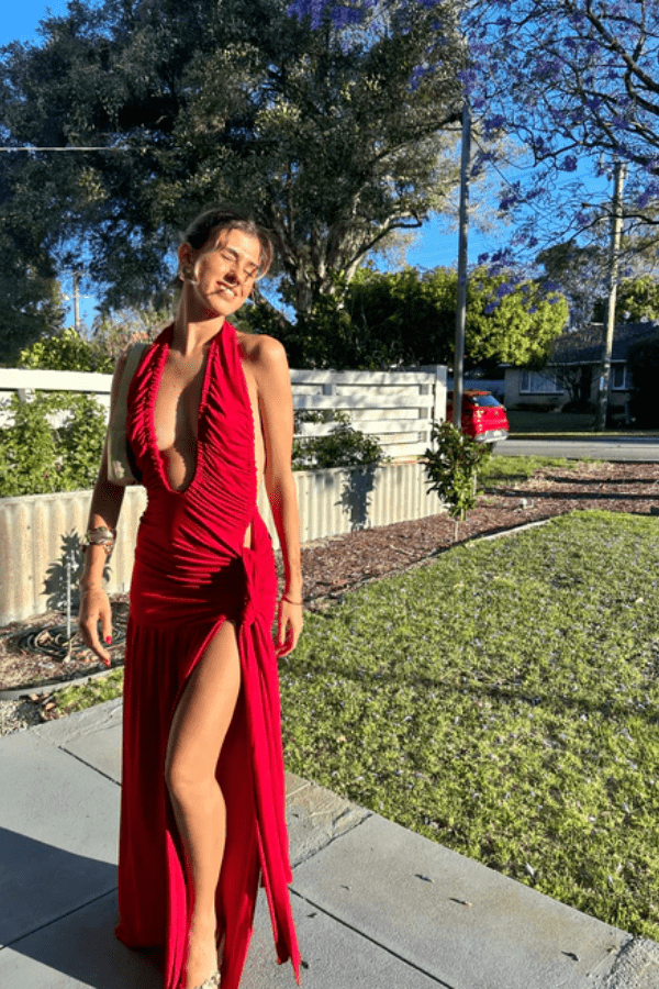 Dakota Pure Red by Deconduarte – Trendy fluid jersey dress with elastic neckline, fitted belt skirt, side slit, and lettuce-edge hem, perfect for confident, carefree occasions.