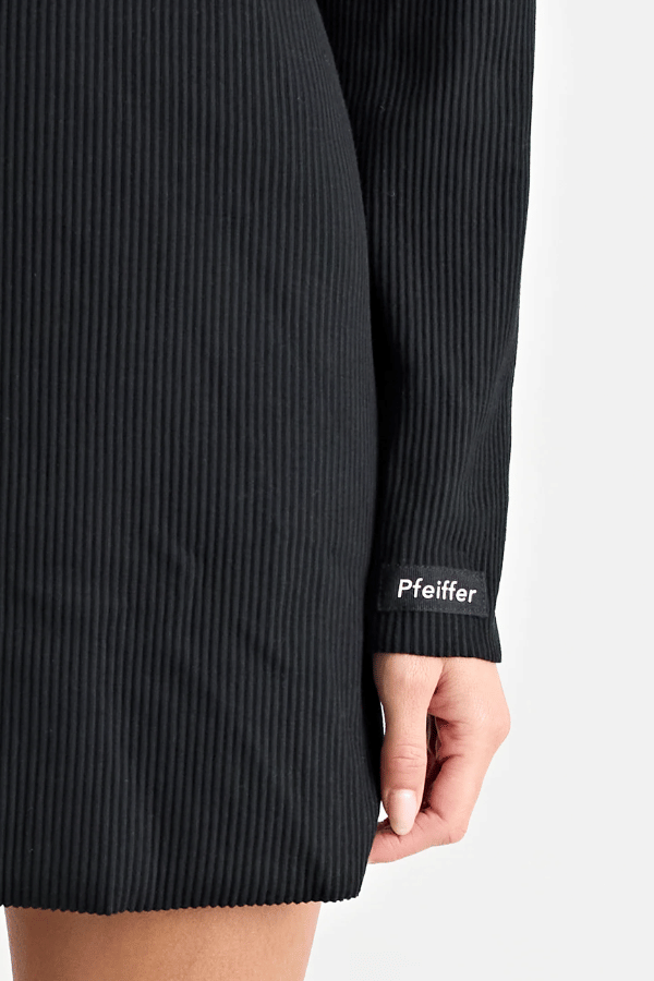 Fairbank Rib Dress Black by Pfeiffer – A trendy, comfortable ribbed bamboo dress with high raw-edge neckline, full sleeves, and versatile two-part back design. Perfect for chic casual wear or layering in cooler seasons.