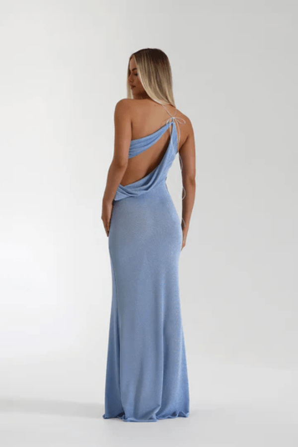 Elissa Dress Periwinkle by Natalie Rolt – A shimmering stretch-knit gown with metallic threads, asymmetrical cutaway, and flowing silhouette, perfect for sophisticated evening events and special occasions.