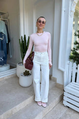 The Polly Long Sleeve top in pink. Woman in a pink top and white pants standing outside a store with plants and a bench in the background.
