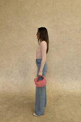 The Polly Long Sleeve top in pink. Woman in a pink top and white pants standing outside a store with plants and a bench in the background.