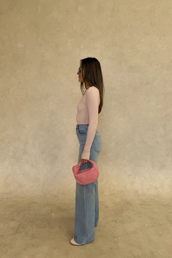 The Polly Long Sleeve top in pink. Woman in a pink top and white pants standing outside a store with plants and a bench in the background.