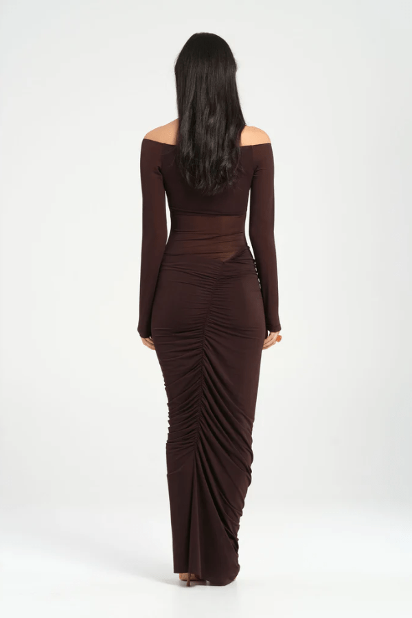 Wilma Maxi Dress Chocolate by Benni, featuring an off-shoulder V-neckline, full-length sleeves, sheer waist, and asymmetrical drape for a sculpted silhouette. Ideal for statement evenings.