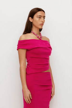Flor Top Magenta by The Wolf Gang — an elegant event-ready top with asymmetric neckline, soft jersey fabric, and delicate beaded strap. True to size, perfect for casual or bold looks.