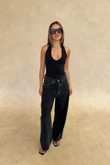 Woman wearing a black sleeveless top and black jeans against a beige background