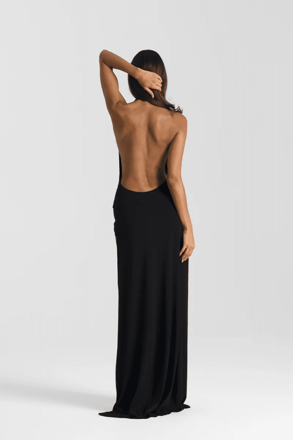 Winona Gown Black by Natalie Rolt, halter neckline, asymmetric draped bust overlay, open back, side split, gathered waterfall skirt, full-length hem, elevated jersey. Dry clean only.