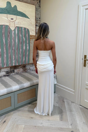 Woman in a white strapless dress standing in a room with a textured wall and bench.