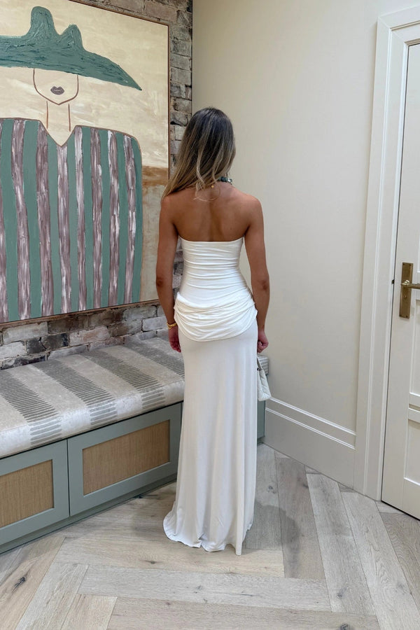 Woman in a white strapless dress standing in a room with a textured wall and bench.