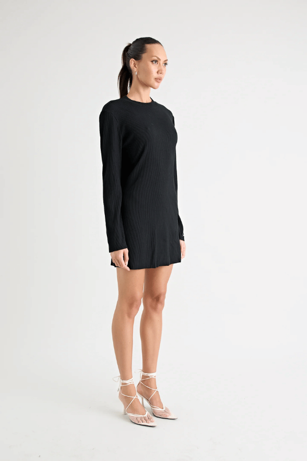 Fairbank Rib Dress Black by Pfeiffer – A trendy, comfortable ribbed bamboo dress with high raw-edge neckline, full sleeves, and versatile two-part back design. Perfect for chic casual wear or layering in cooler seasons.