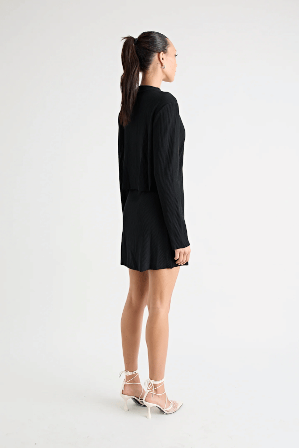 Fairbank Rib Dress Black by Pfeiffer – A trendy, comfortable ribbed bamboo dress with high raw-edge neckline, full sleeves, and versatile two-part back design. Perfect for chic casual wear or layering in cooler seasons.