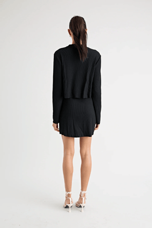 Fairbank Rib Dress Black by Pfeiffer – A trendy, comfortable ribbed bamboo dress with high raw-edge neckline, full sleeves, and versatile two-part back design. Perfect for chic casual wear or layering in cooler seasons.