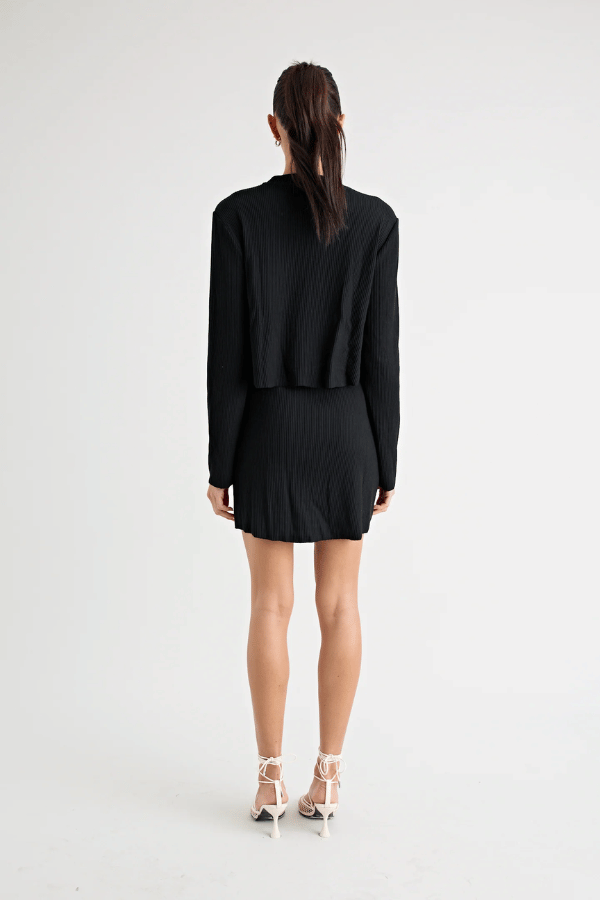 Fairbank Rib Dress Black by Pfeiffer – A trendy, comfortable ribbed bamboo dress with high raw-edge neckline, full sleeves, and versatile two-part back design. Perfect for chic casual wear or layering in cooler seasons.