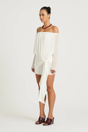Bernie Mini Dress by Benni, white off-shoulder mini with long sleeves, draped front, waist tie and sheer feminine silhouette.