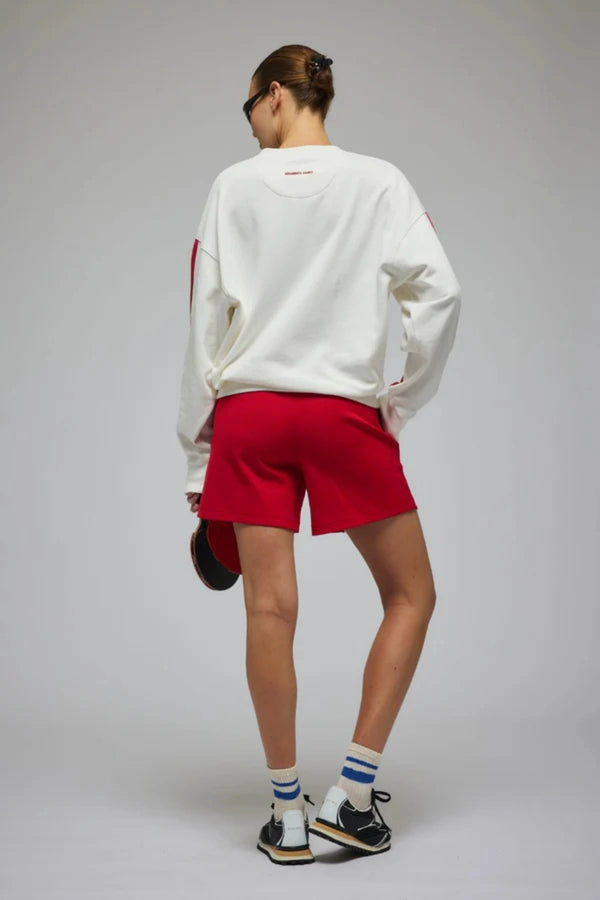 Club Med Sweatshirt in Warm White by Araminta James, soft cotton fleece with red sleeve panels and velvet chest applique, relaxed fit for chic off-duty or travel styling.