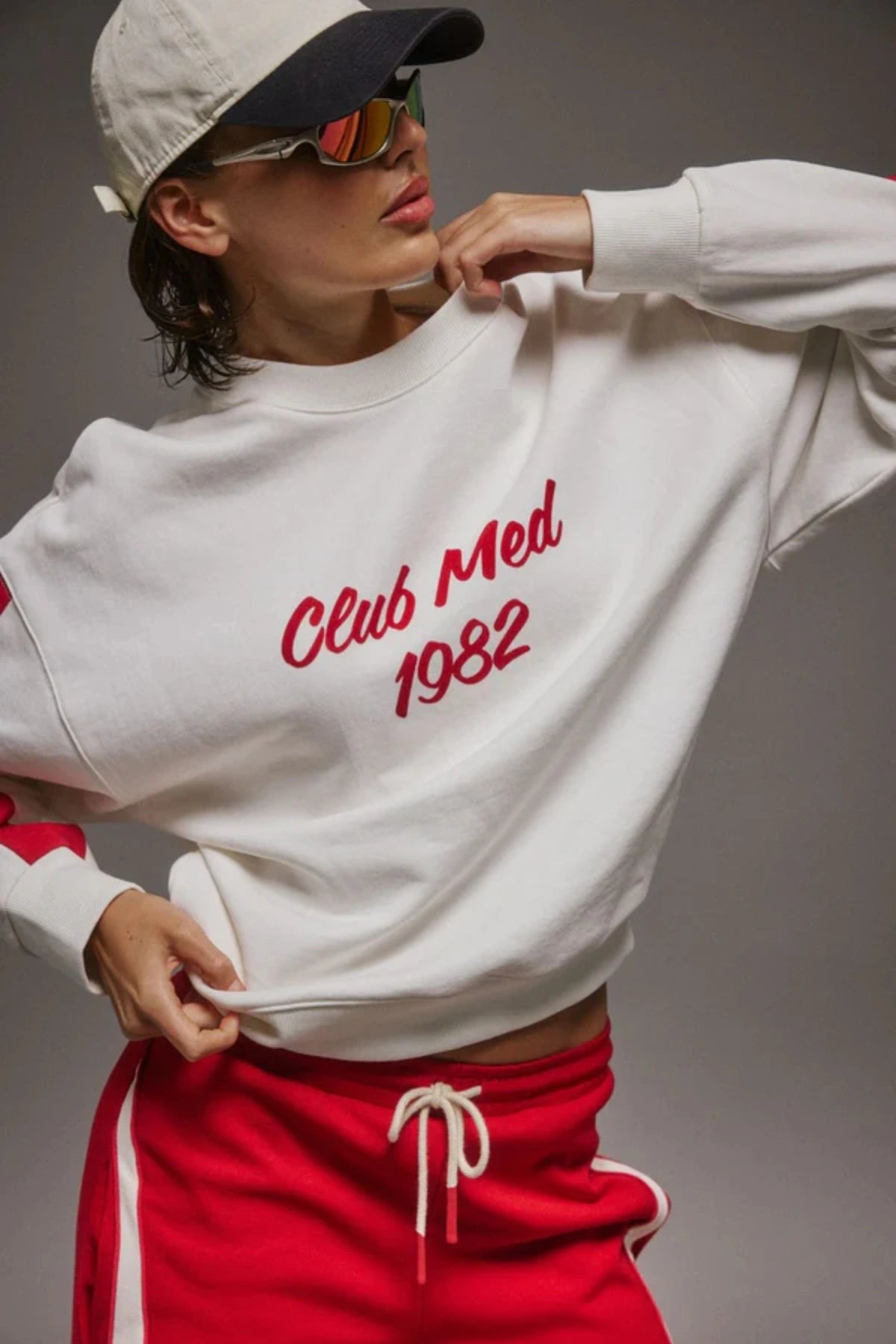 Club Med Sweatshirt in Warm White by Araminta James, soft cotton fleece with red sleeve panels and velvet chest applique, relaxed fit for chic off-duty or travel styling.