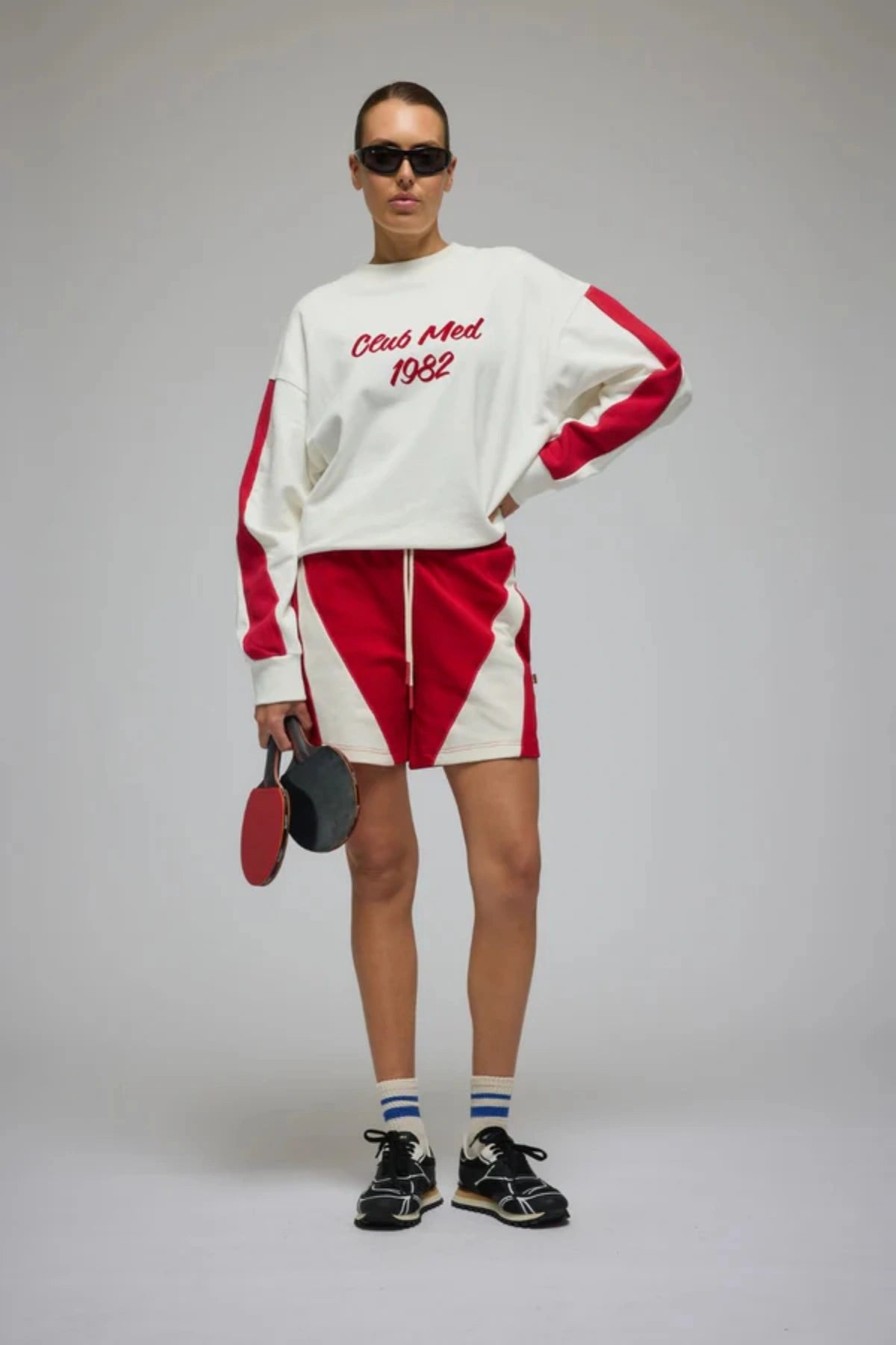 Club Med Sweatshirt in Warm White by Araminta James, soft cotton fleece with red sleeve panels and velvet chest applique, relaxed fit for chic off-duty or travel styling.