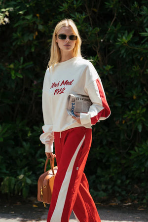 Club Med Sweatshirt in Warm White by Araminta James, soft cotton fleece with red sleeve panels and velvet chest applique, relaxed fit for chic off-duty or travel styling.