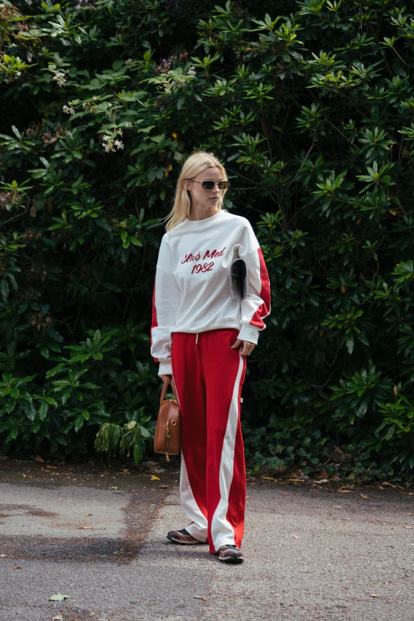 Club Med Sweatshirt in Warm White by Araminta James, soft cotton fleece with red sleeve panels and velvet chest applique, relaxed fit for chic off-duty or travel styling.