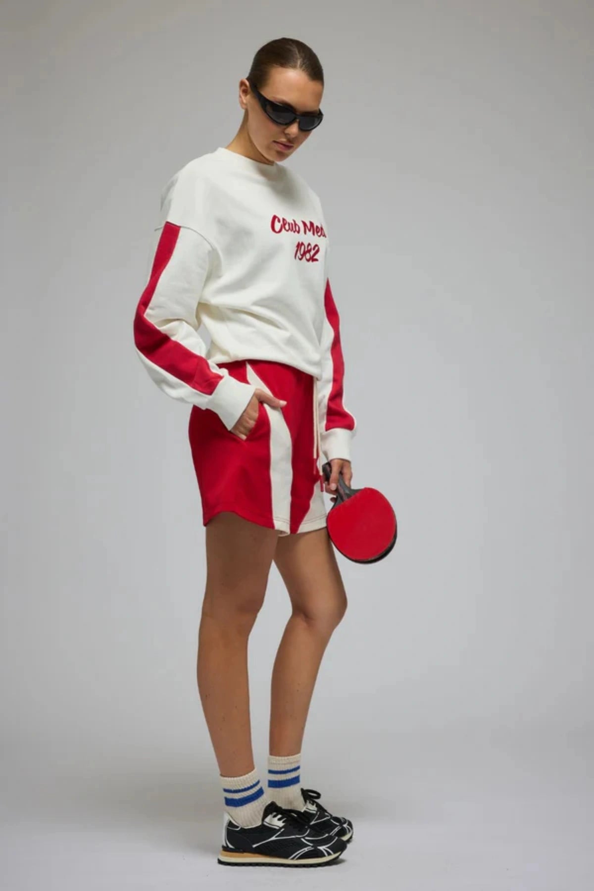 Club Med Sweatshirt in Warm White by Araminta James, soft cotton fleece with red sleeve panels and velvet chest applique, relaxed fit for chic off-duty or travel styling.