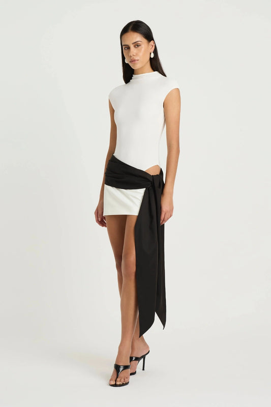 Dakota Mini Dress by Benni, a white mini with cap sleeves and asymmetric tie detail. Perfect for polished summer days or events.