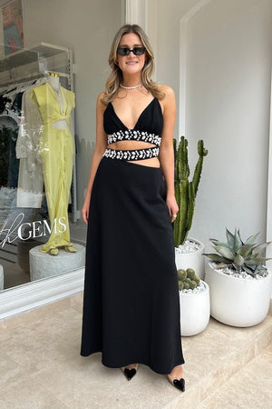 La Playa Maxi Dress Noir by The Wolf Gang – Maxi dress with cowrie shell cutouts, adjustable tie, and luxe gold clasp closure.