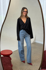 Woman in black top and blue jeans standing in front of a mirror.