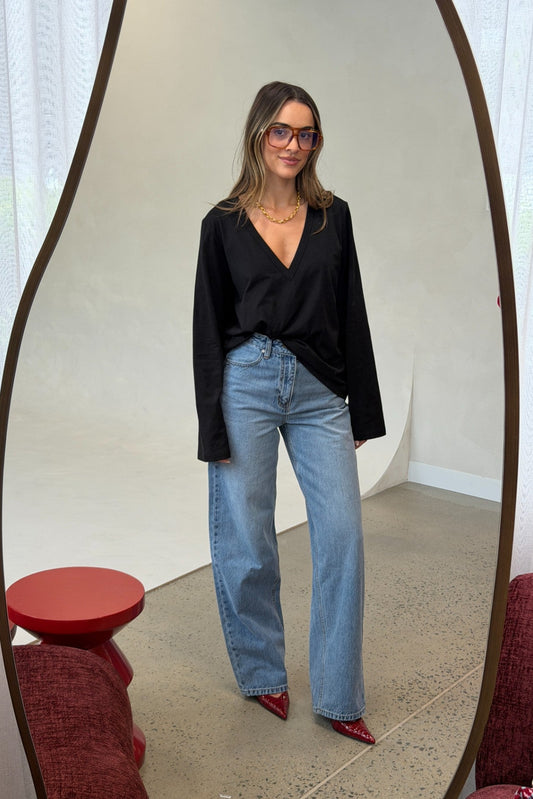 Woman in black top and blue jeans standing in front of a mirror.