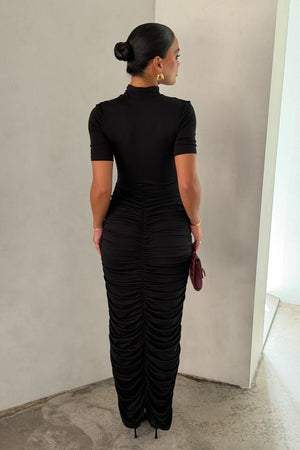 The Imana Draped Maxi Dress in Black by Sneaky Link features a flattering draped skirt, fitted upper, and soft modal stretch fabric for a feminine, timeless silhouette.