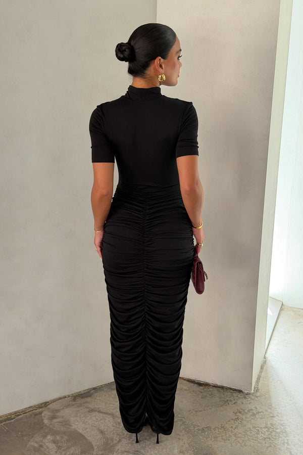 The Imana Draped Maxi Dress in Black by Sneaky Link features a flattering draped skirt, fitted upper, and soft modal stretch fabric for a feminine, timeless silhouette.