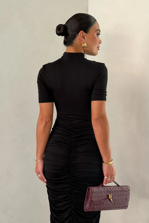 The Imana Draped Maxi Dress in Black by Sneaky Link features a flattering draped skirt, fitted upper, and soft modal stretch fabric for a feminine, timeless silhouette.