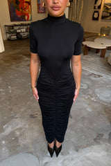 The Imana Draped Maxi Dress in Black by Sneaky Link features a flattering draped skirt, fitted upper, and soft modal stretch fabric for a feminine, timeless silhouette.