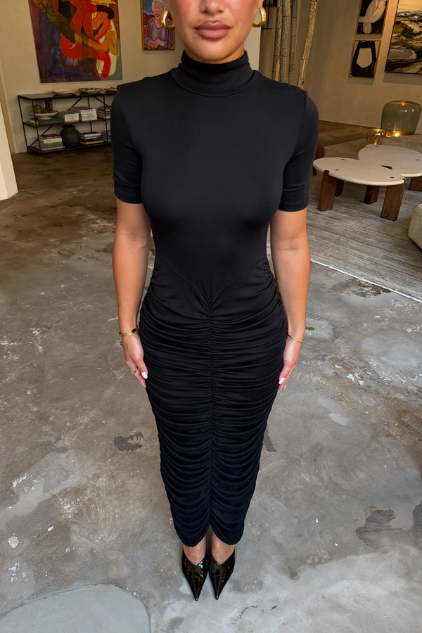 The Imana Draped Maxi Dress in Black by Sneaky Link features a flattering draped skirt, fitted upper, and soft modal stretch fabric for a feminine, timeless silhouette.