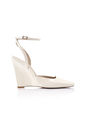 Lana Wilkinson Mona Wedge in glossy ivory patent leather with pointed toe, ankle strap, and sculptural wedge heel.